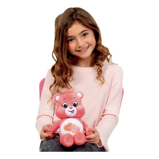Girl happily, holding a pink plush care bear on her knee