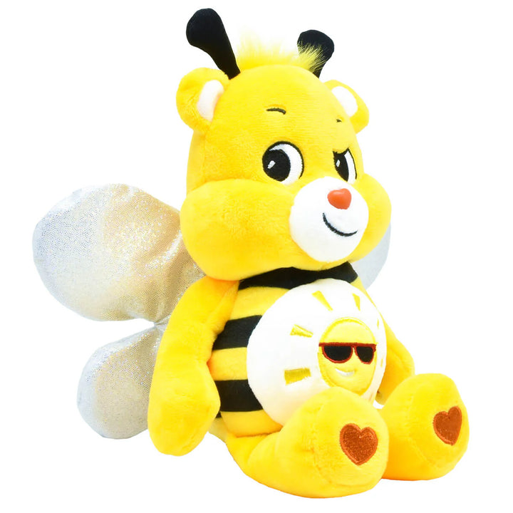 A yellow and black striped plush bee toy with white wings, a white snout, and embroidered heart details on its feet, shown against a plain white background. A Care Bear with bee features and a sun on its tummy